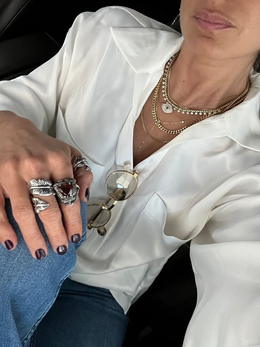 Mujer con blusa blanca de botones usando diferentes anillos llamativos en una mano y diferentes collares en capas
